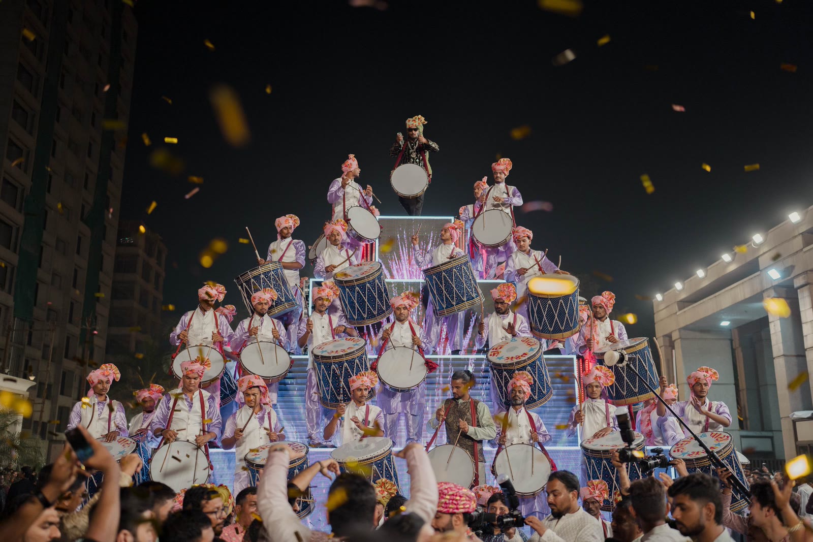A dhol troupe banked in a pyramid at night with gold confetti falling