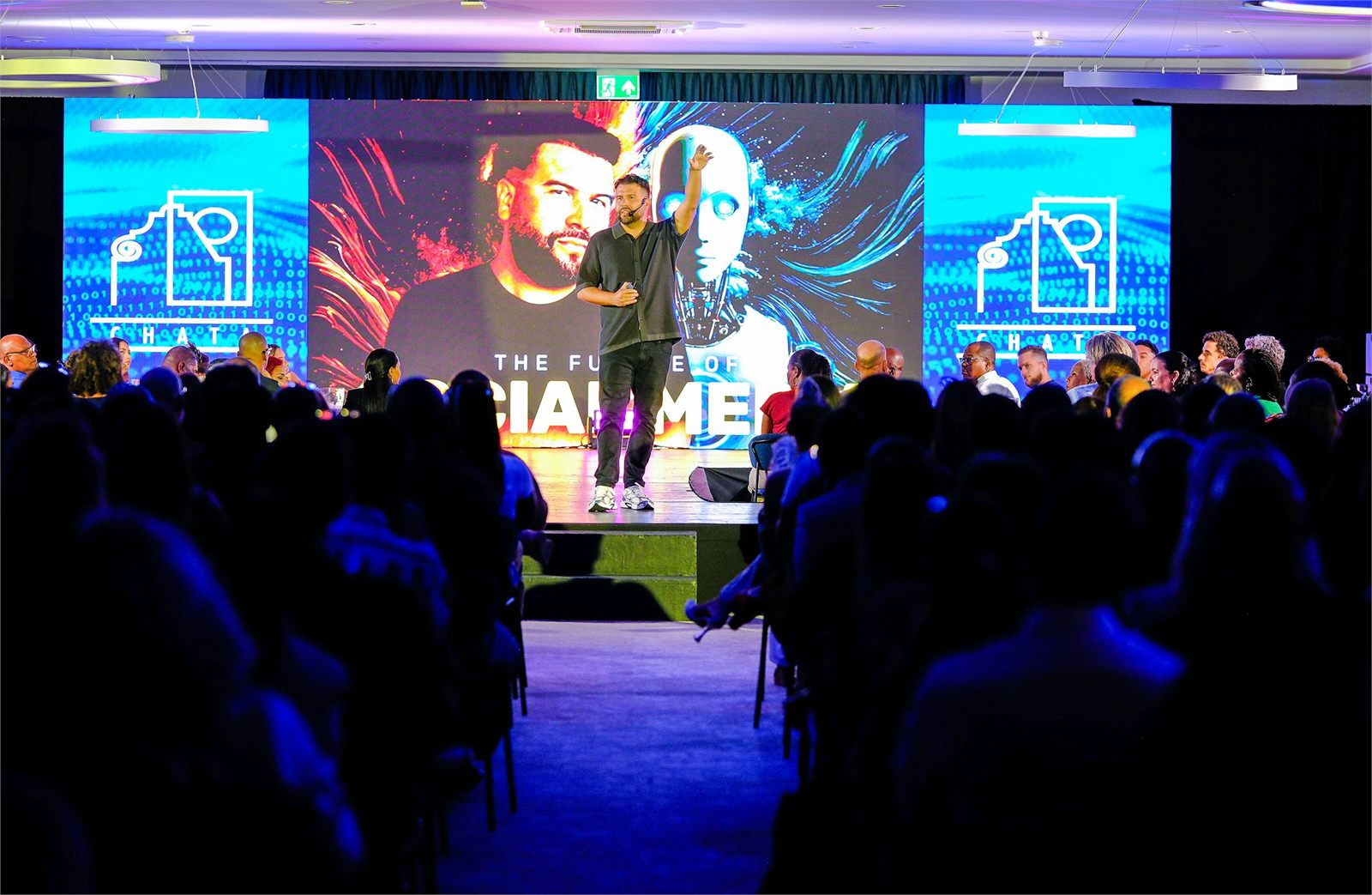 A speaker presenting on a lit stage to a seated audience