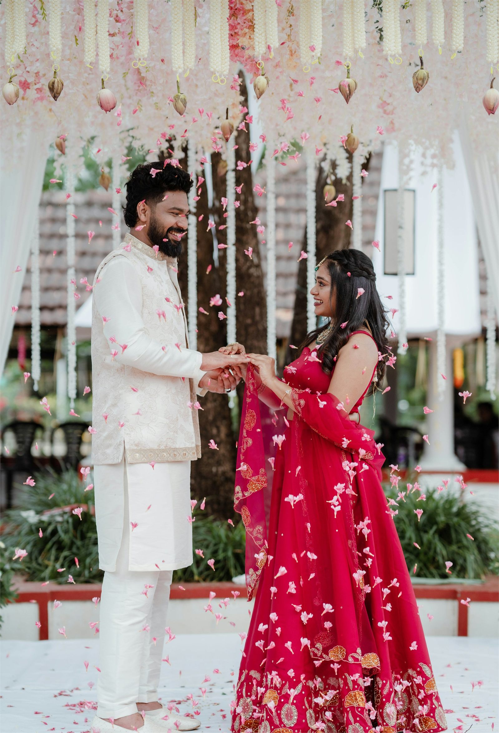 A couple exchanging rings beneath a floral canopy as petals fall around them