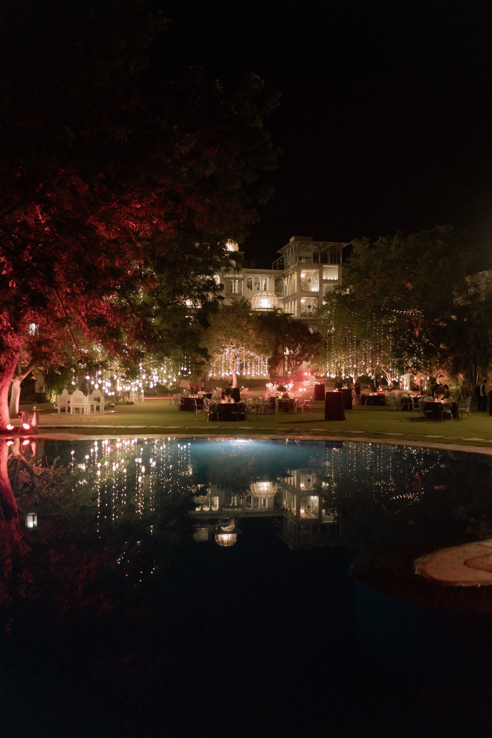 A night garden reception with fairy-lit trees mirrored in a pool