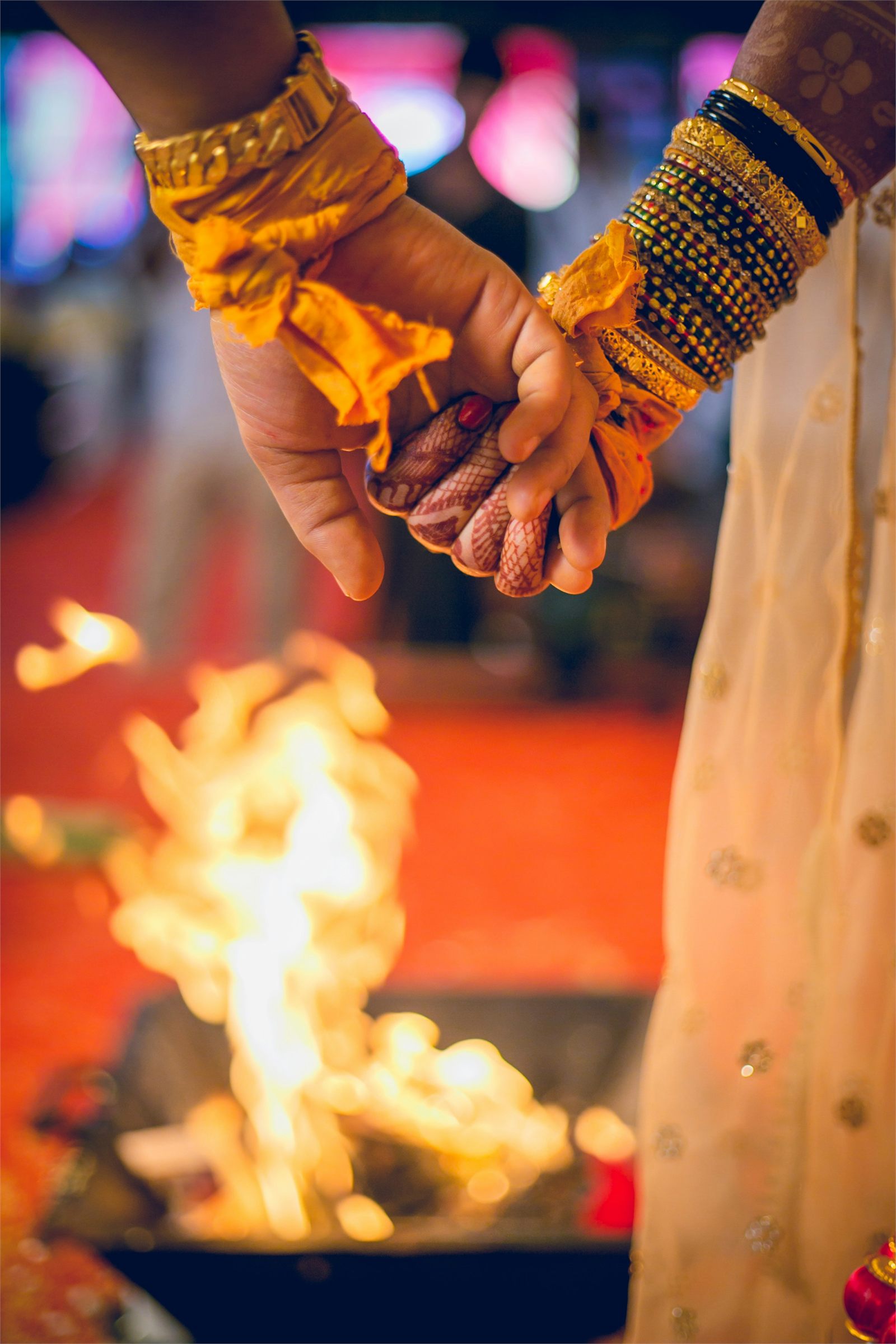 Two hands bound with turmeric cloth and gold bangles held above the sacred fire