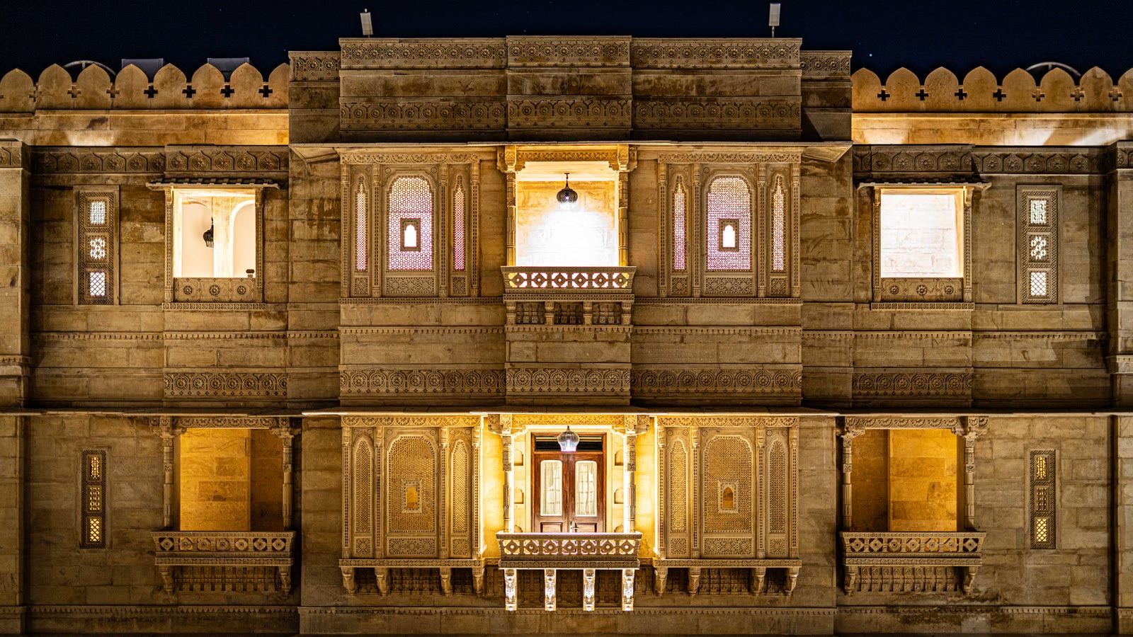 The carved sandstone facade of a heritage palace hotel lit warmly at night