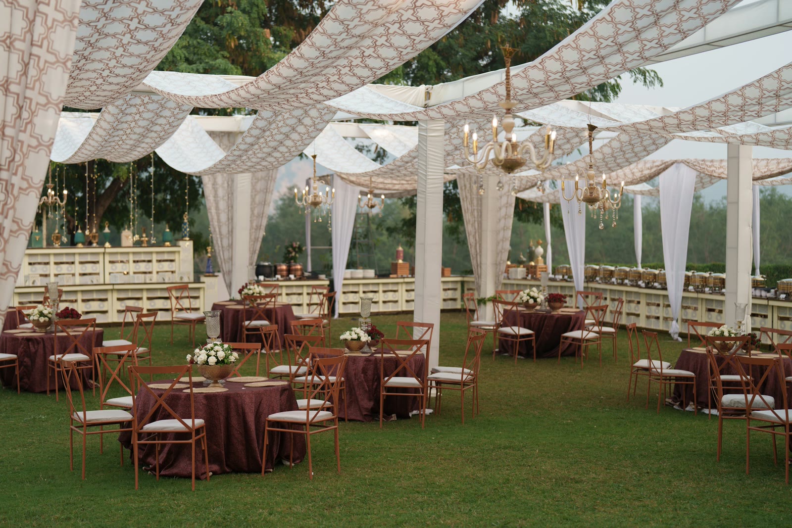 An outdoor reception beneath a draped canopy and chandeliers