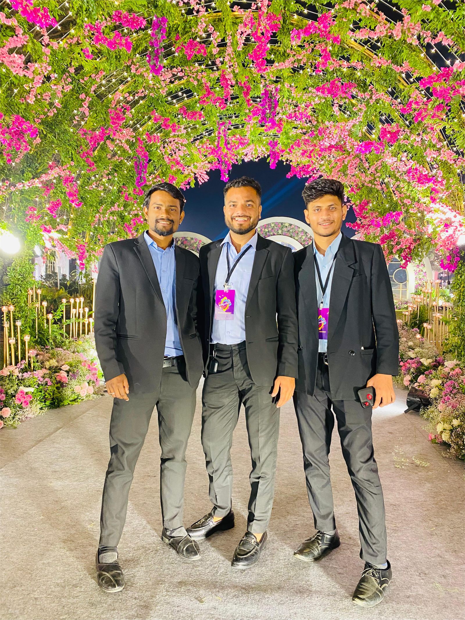 Three Indraa Events crew members beneath a floral entrance arch strung with fairy lights