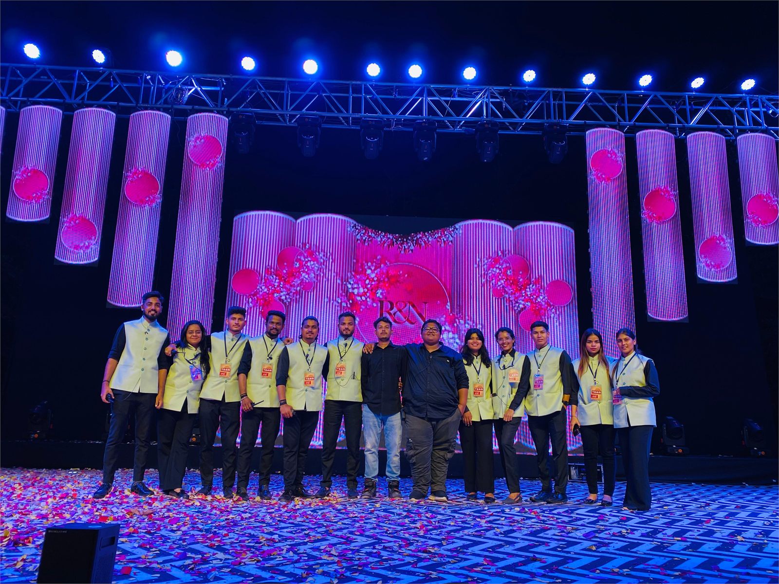 Indraa Events crew on a sangeet stage with an LED backdrop and confetti across the floor